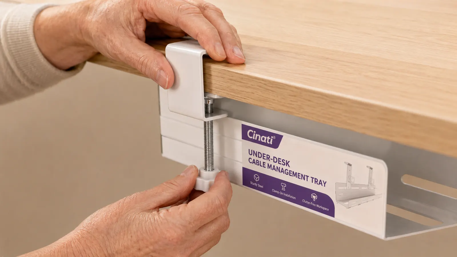 Hands attaching a white cable management tray clamp underneath a desk edge