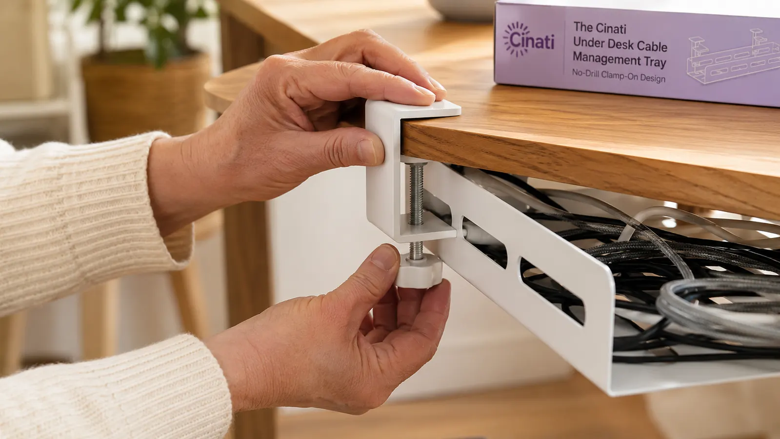 Hands attaching a white cable management tray clamp to the underside of a desk