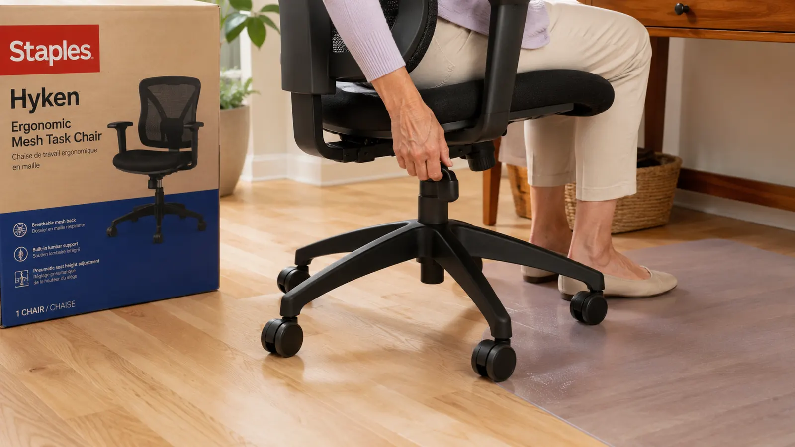 Close-up of the Staples Hyken chair caster wheels on a hardwood floor with a chair mat visible underneath